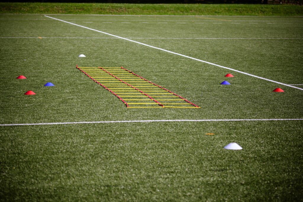 Agility ladder and marker cones set up on a grassy football field for training.