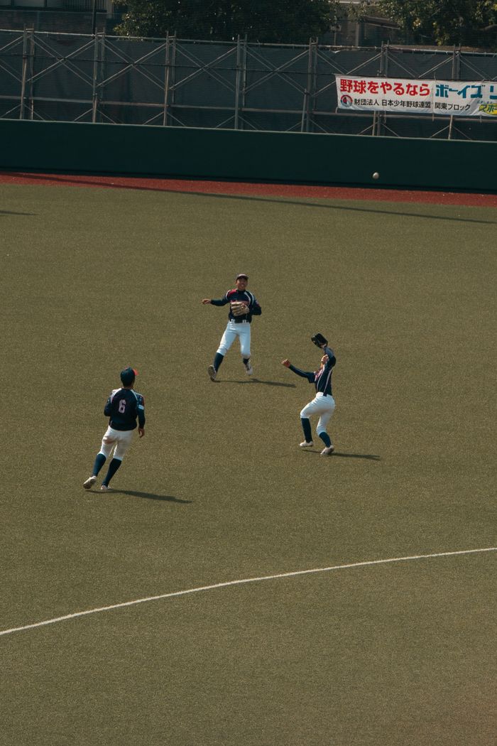 Three young baseball players in action during a game on an outdoor field in Tokyo.