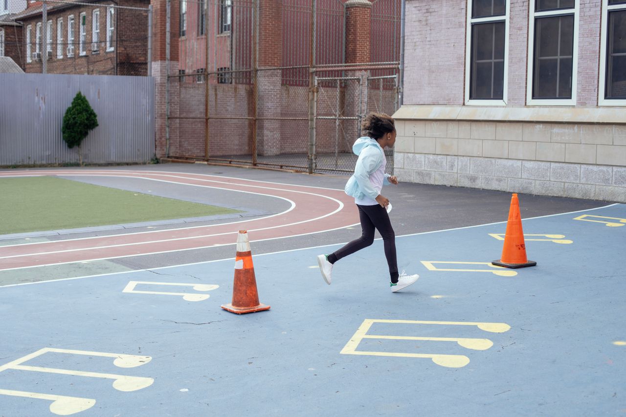 Side view of African American kid in sportswear doing running exercise with red cones during outdoors gym class in backyard of school in daytime